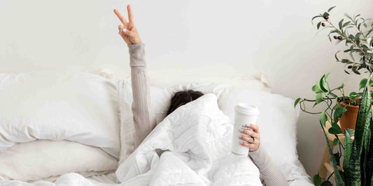 Woman in bed under her duvet holding a cup of coffee and Bedtime Ritual Guide