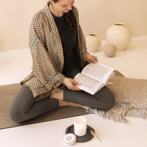 Someone reading the Morning Notes - Daily wellbeing journal LSW on a yoga matt with shō-moon meditation candle